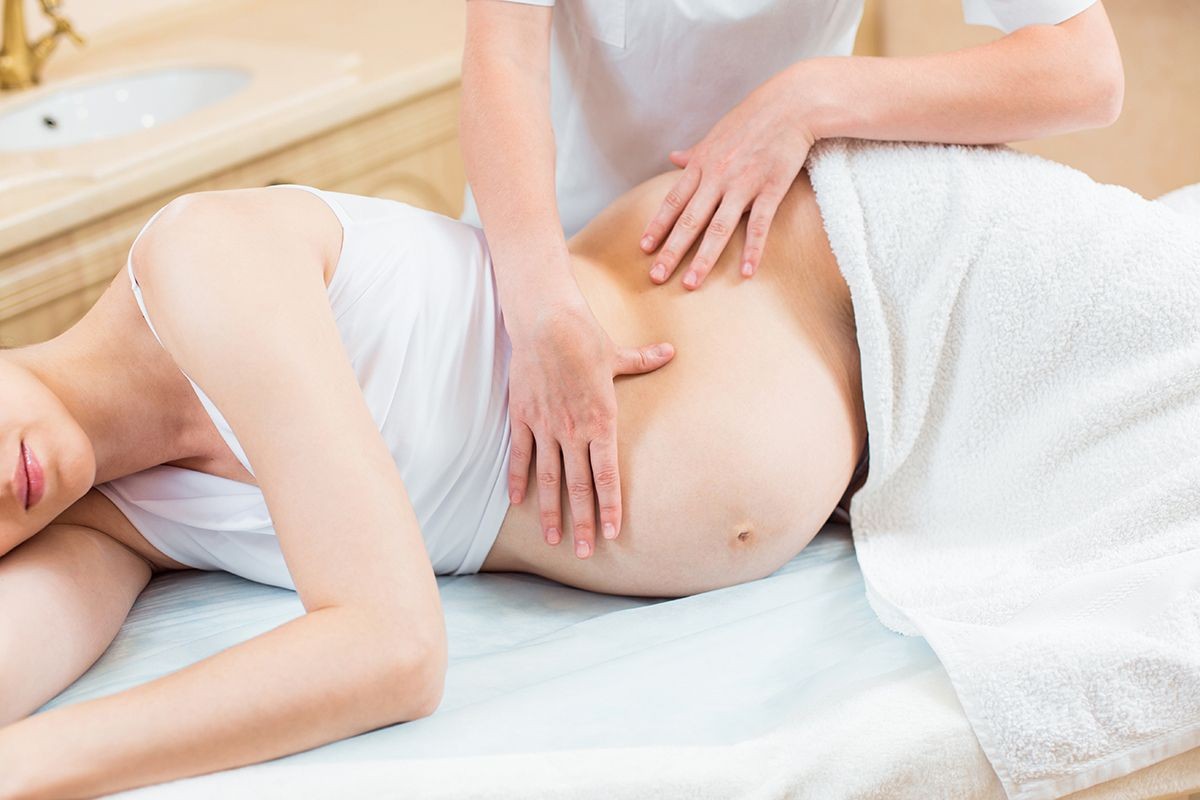 Pregnant woman lying on her side receiving a massage on her back and abdomen from a professional.